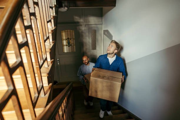 Twee mensen dragen samen een verhuisdoos een trap op. Intrek in een eigen woning.